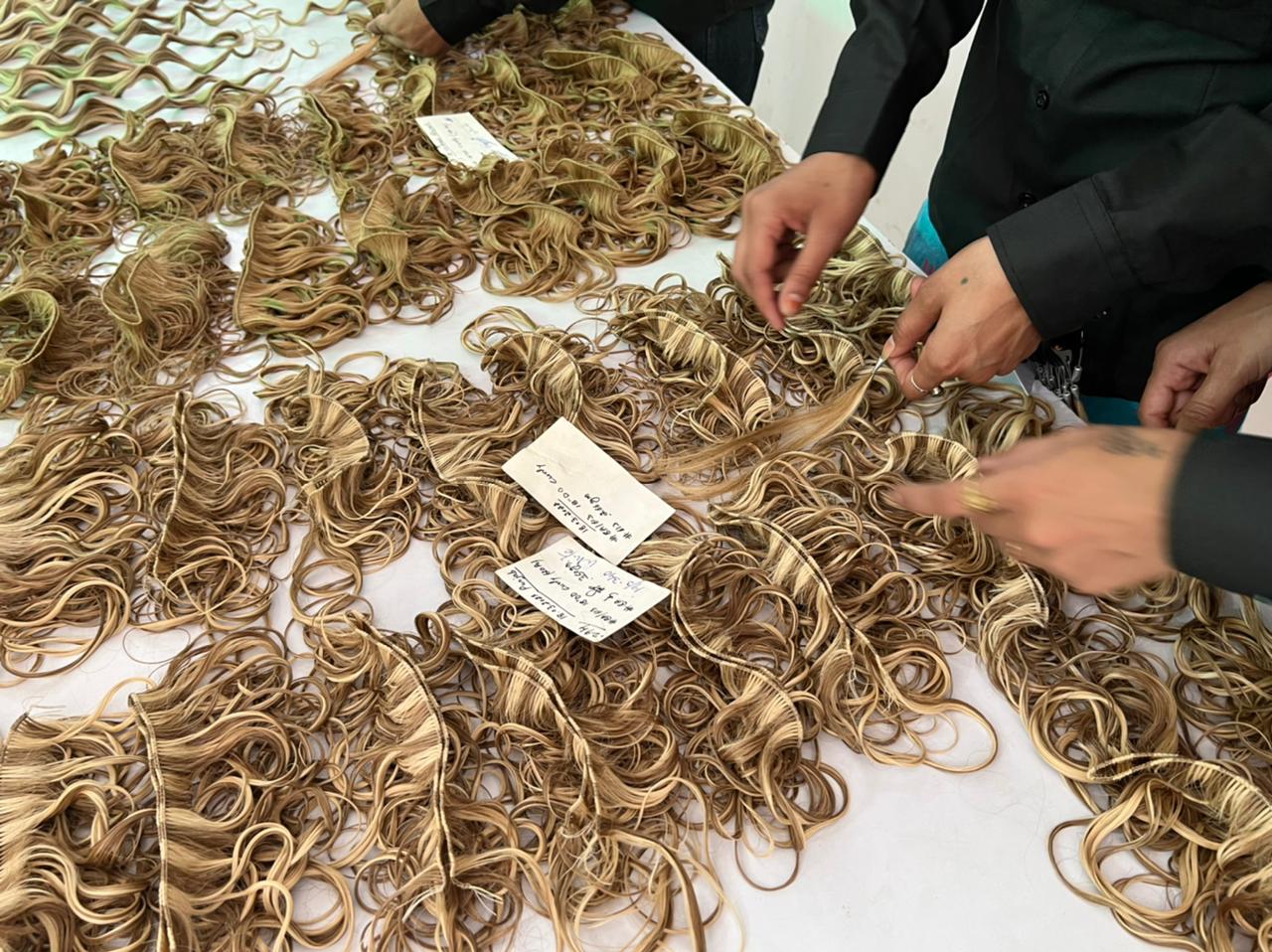 Rows of rooted beige and honey blonde wefts laid out with handwritten batch tickets