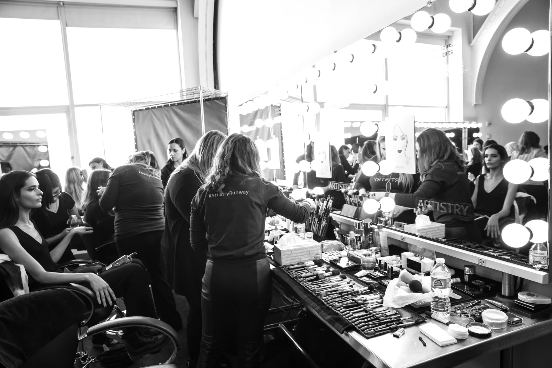 Backstage make-up counter under bulb mirrors with brushes laid out in rows