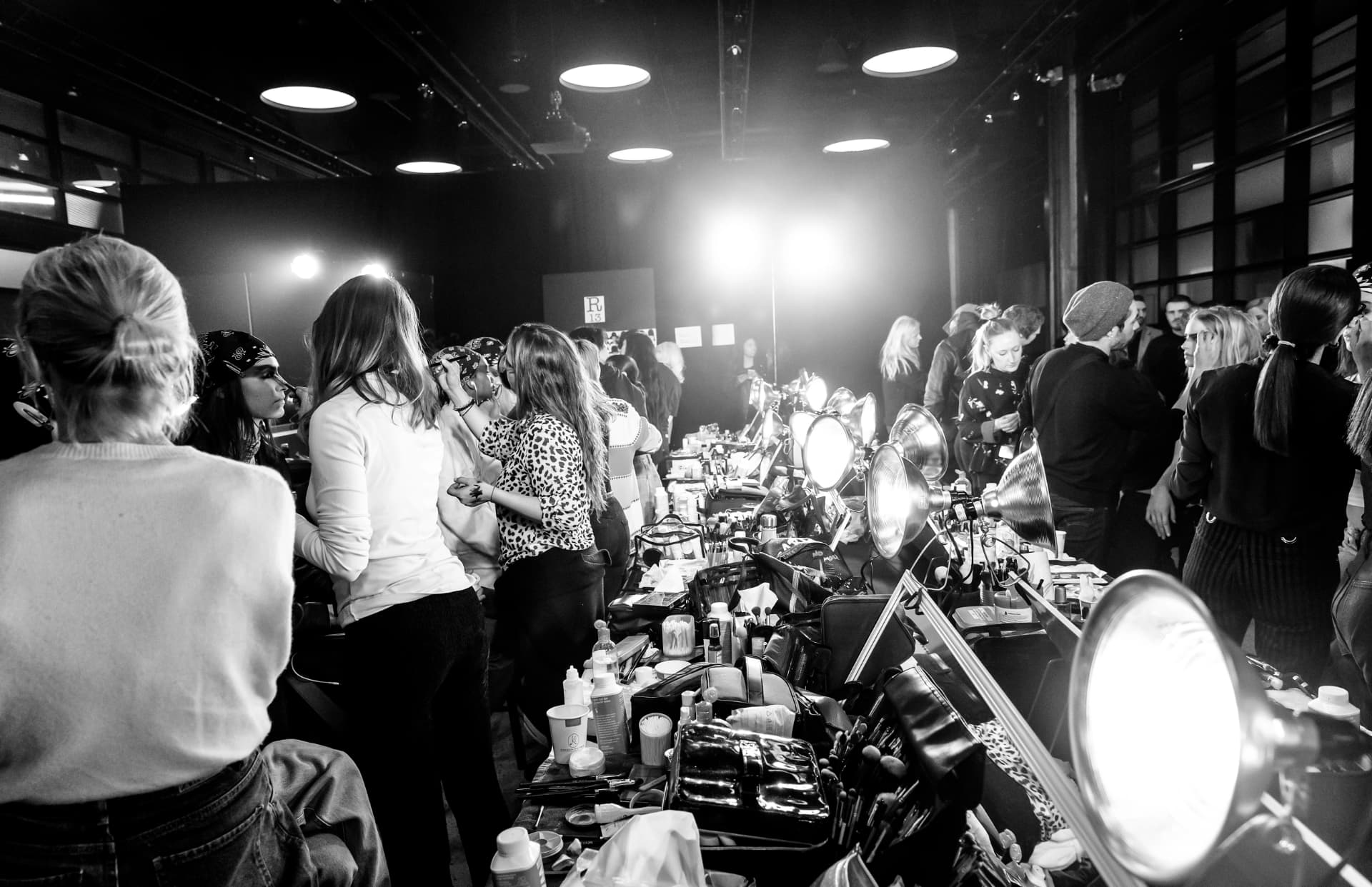 Crowded backstage benches with lamps, kits and stylists at work
