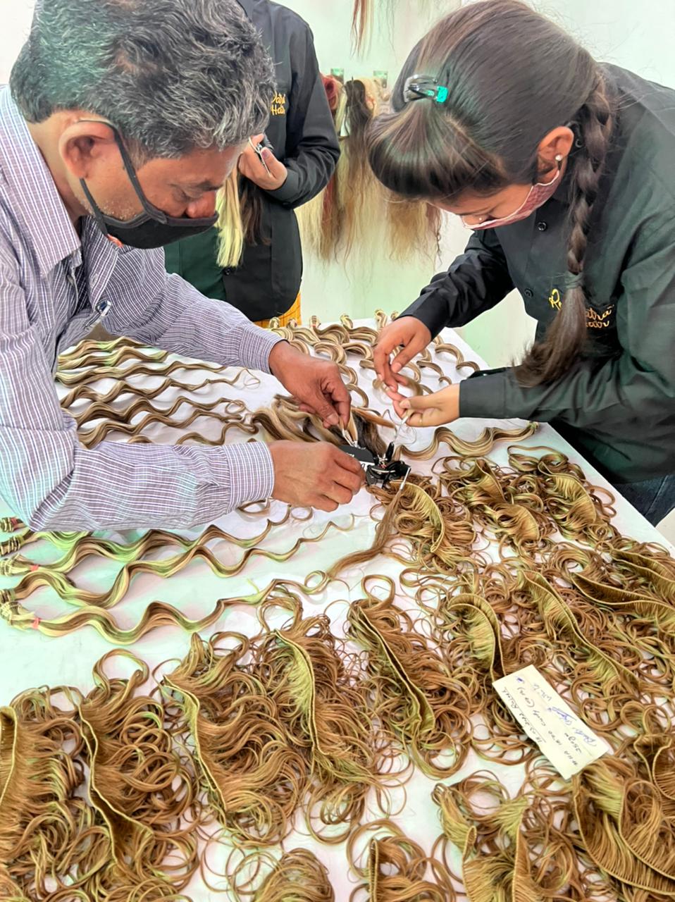 Two RemyPatra colour technicians checking a rooted blonde weft strand by strand