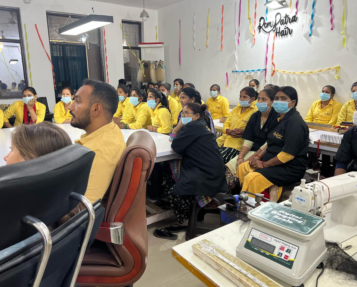 RemyPatra factory team in yellow uniforms at a training session, with the digital weighing scale and sewing station in front